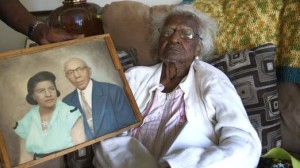 Talley sits on her couch, as a photograph showing her and her late husband Alfred is held next to her, on her 115th birthday in her home in Inkster