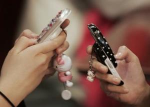 Middle-school girls use mobile phones as they chat in a restaurant in Seoul